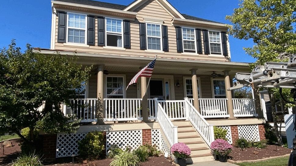 Two-story colonial house with beige siding, white porch railing and American flag