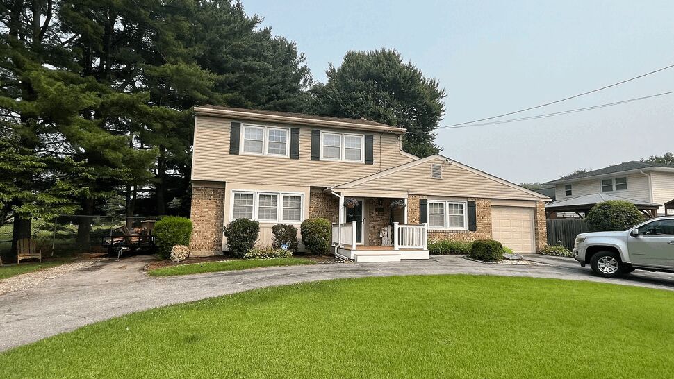 Colonial siding and roofline | Tycos Roofing And Siding Inc Two-story colonial house with beige siding, brick accents, and front porch
