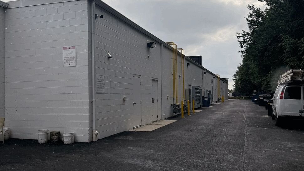 Long alley beside a white commercial building with flat roof and asphalt under cloudy sky.