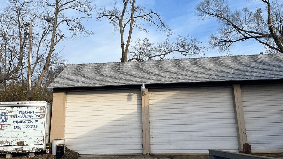 Gray shingled roof above three white garage doors at a commercial building