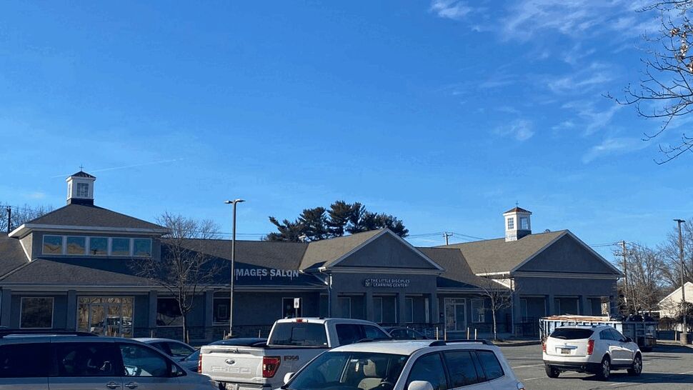Commercial storefront with parking lot and shingled roofs under blue sky