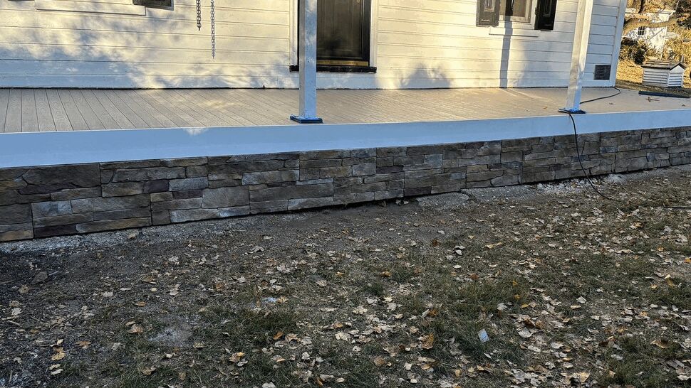 Finished porch with composite decking and stone skirting on a white house
