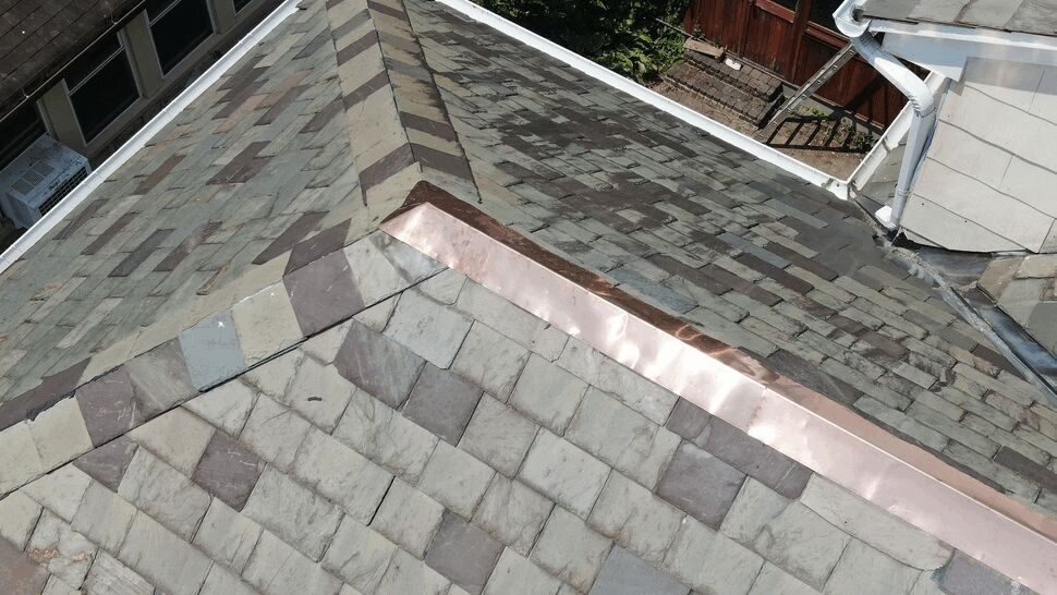 Close-up of copper ridge flashing installed on slate roof tiles.