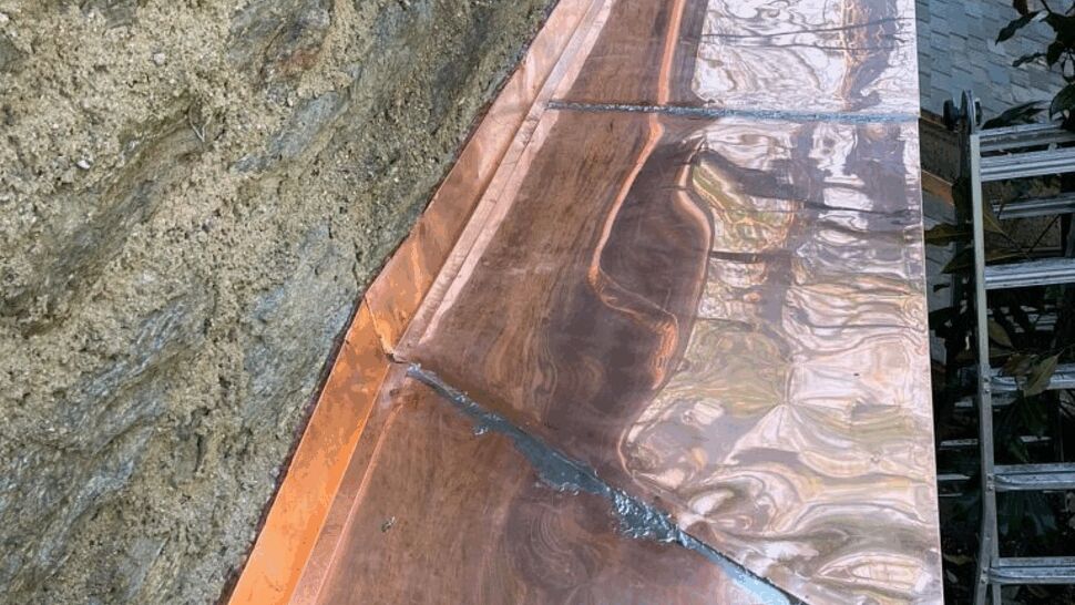 Shiny copper flashing over a window ledge on stone wall