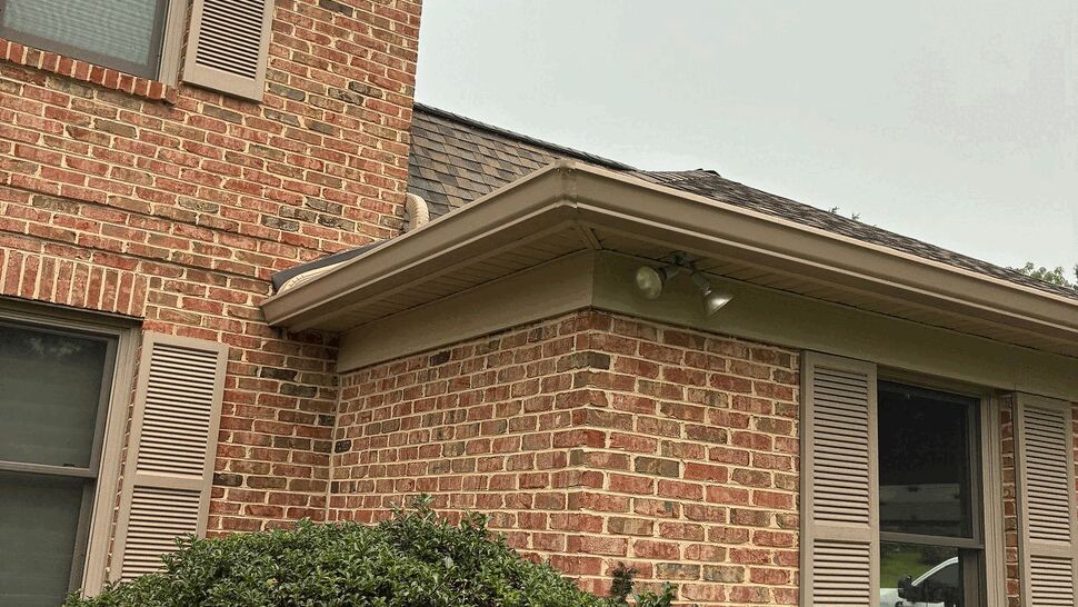 Close-up of a roof corner, soffit and downspout over a brick wall.