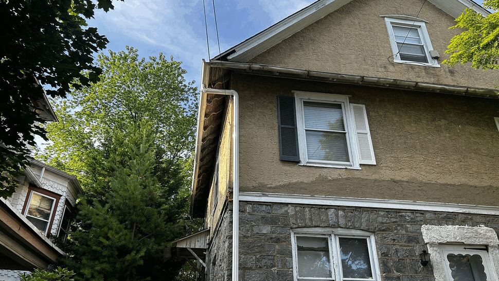 House corner with white downspout, stone lower facade, and upper stucco under eaves