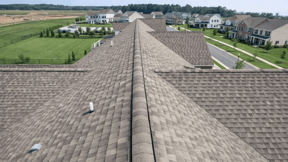 Aerial view along a long shingle roof ridge over suburban homes