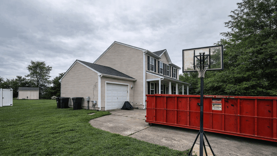 Driveway Dumpster for Storm Cleanup | Tycos Roofing And Siding Inc Driveway with red dumpster, garage, and a portable basketball hoop during cleanup