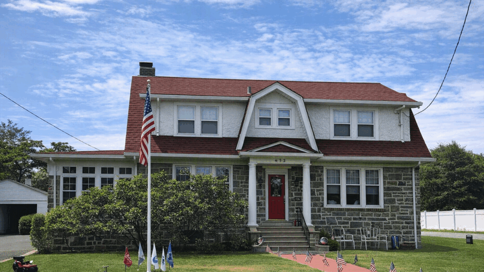 Two-story stone-front house with red shingle roof and flagpole
