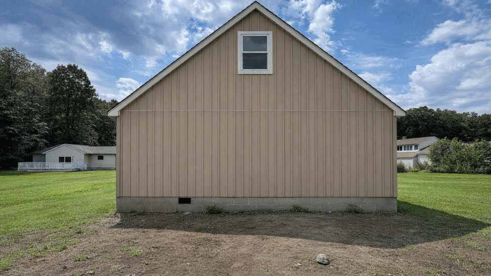 Beige gable end with small upper window and vertical siding under a partly cloudy sky