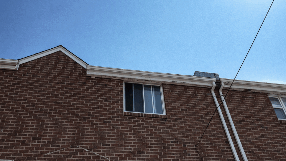 Second-floor brick wall with window and gutters under blue sky