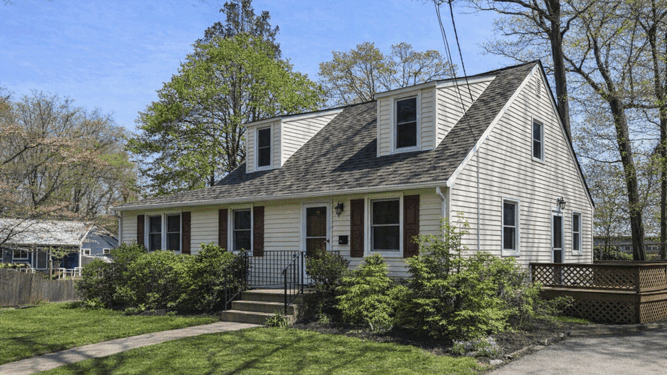Front view of a white cape-style home with dormers and a shingled roof