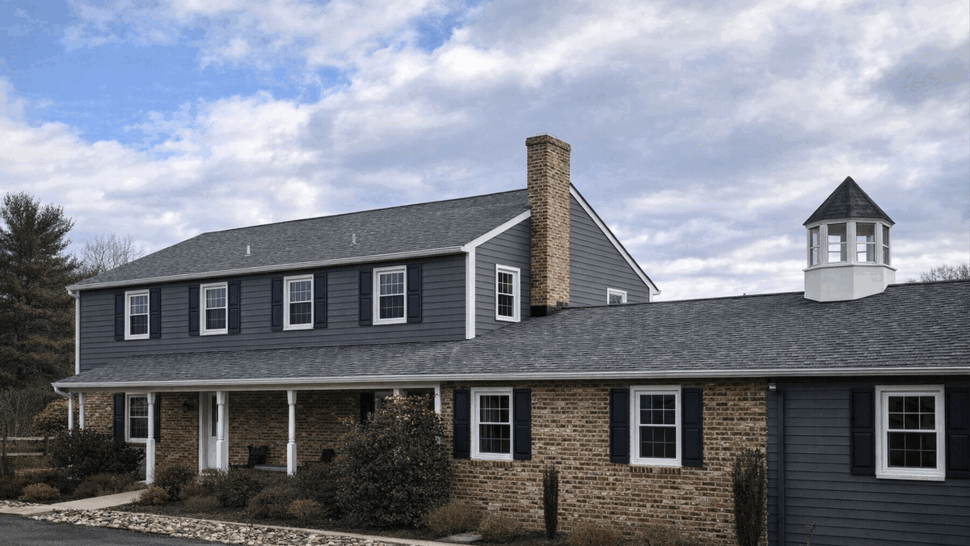 Side view of home showing siding, chimney, and roof cupola against cloudy sky.