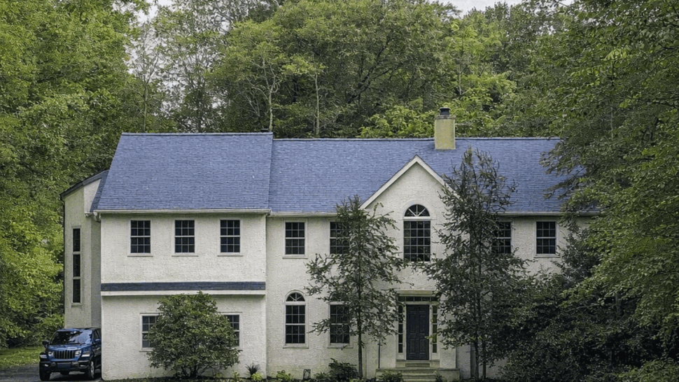 Two-story home with blue shingle roof | Tycos Roofing And Siding Inc Two-story colonial home with blue shingle roof set among trees.