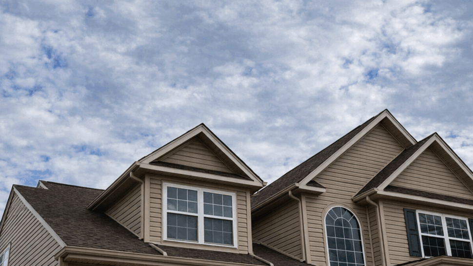 Close-up of gable roofline, dormer windows and gutters beneath a cloudy sky.