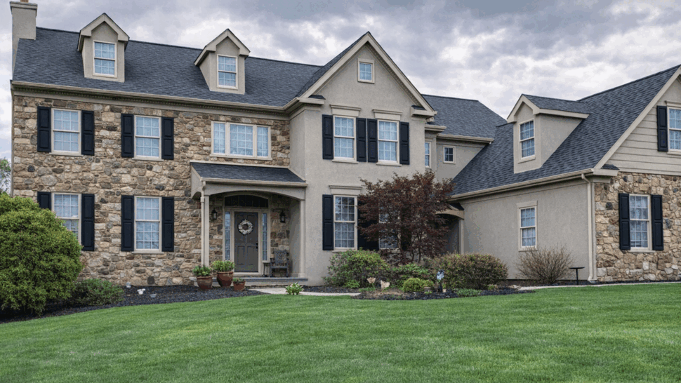 Two-Story Stone and Stucco Home Exterior | Tycos Roofing And Siding Inc Two-story stone and stucco home with dark shingled roof and green lawn.
