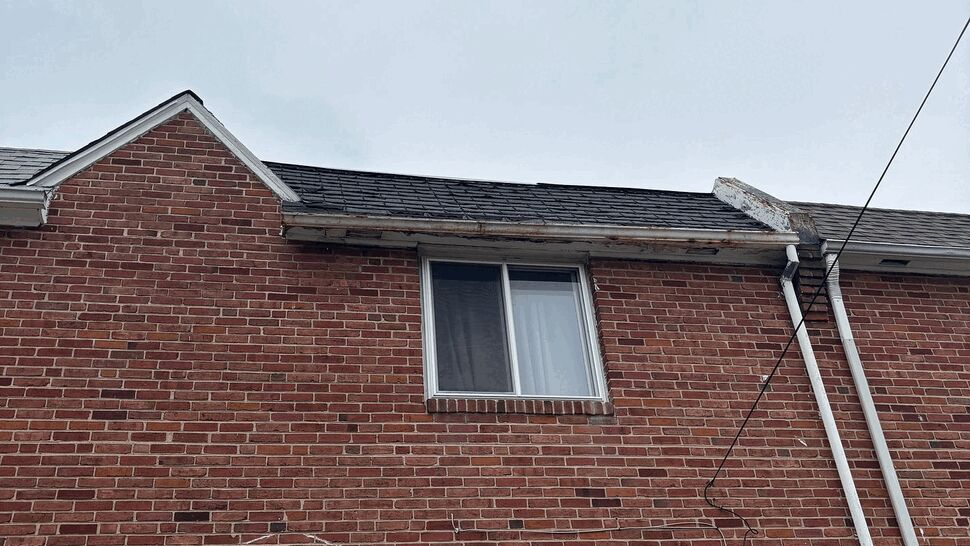 Upper facade showing peeling eave trim and roofline above a second-story window.