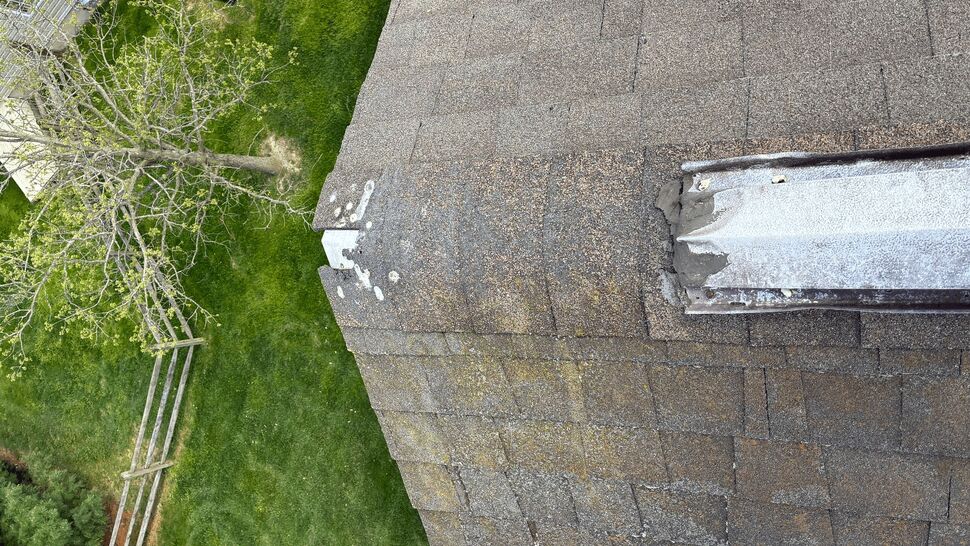 Close-up of a damaged ridge cap with worn shingles and exposed underlayment