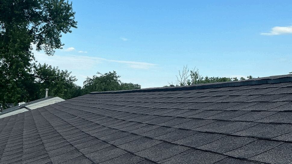 Close-up view of dark asphalt roof shingles stretching toward the horizon.