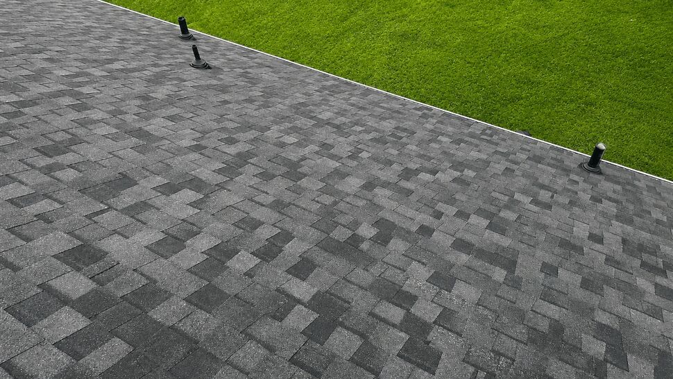 Close-up of dark gray asphalt shingles with roof vents and green lawn