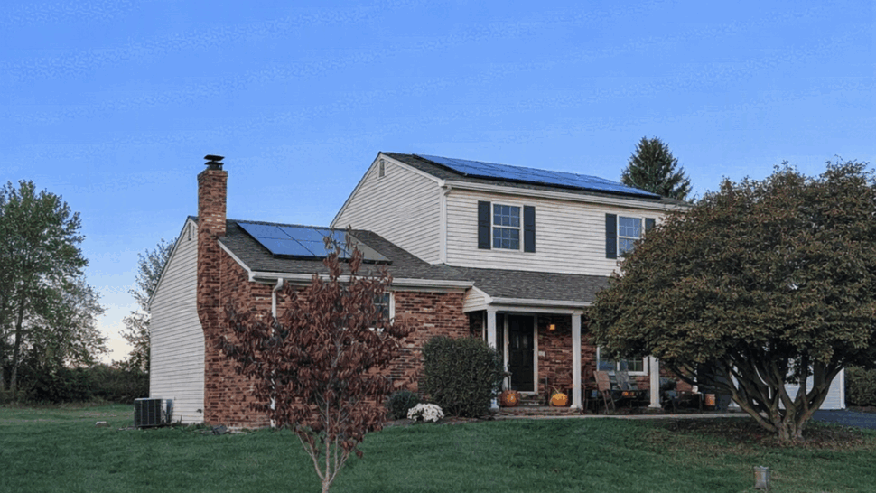 Two-story house with shingle roof and solar panels, front lawn