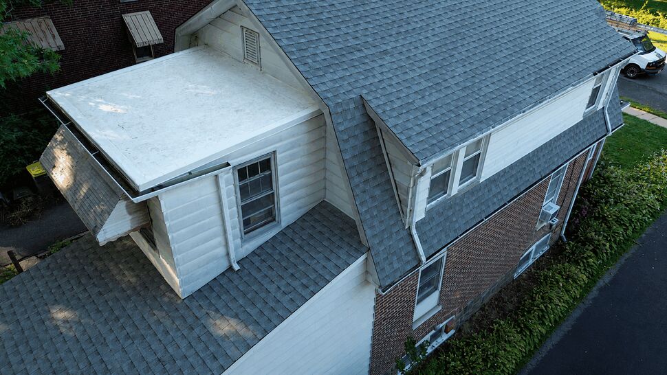 Close aerial of a dormer, small flat roof section and adjoining grey shingled roof.