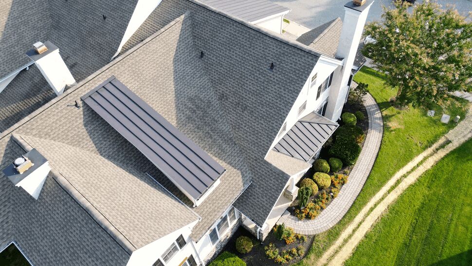 Drone image of shingled roof edge showing gutters, front landscaping, and driveway.