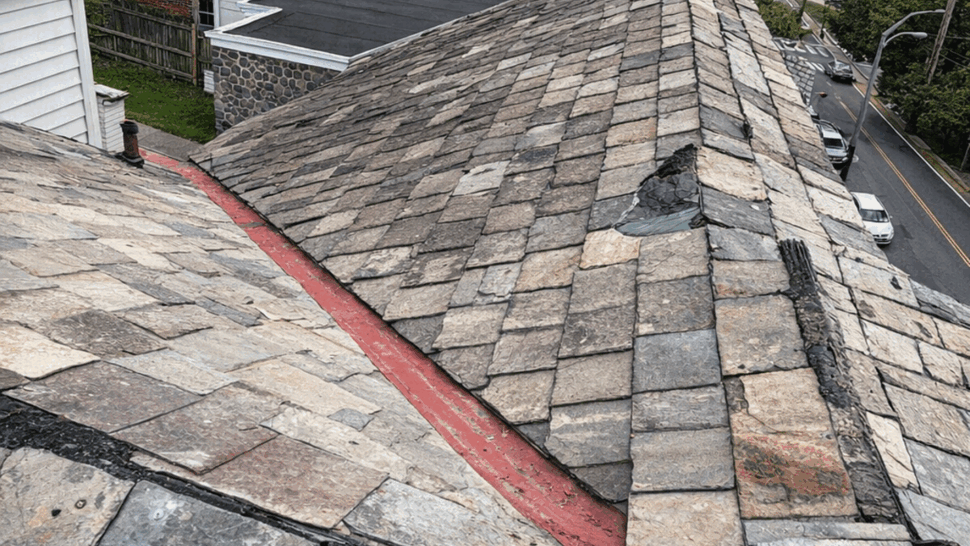 Aging slate roof valley inspection | Tycos Roofing And Siding Inc Aerial view of an aging slate roof valley with visible flashing and worn tiles