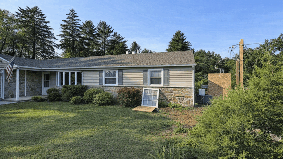 Ranch home siding and window view | Tycos Roofing And Siding Inc Front of ranch house with stone and vinyl siding and a loose window on the lawn