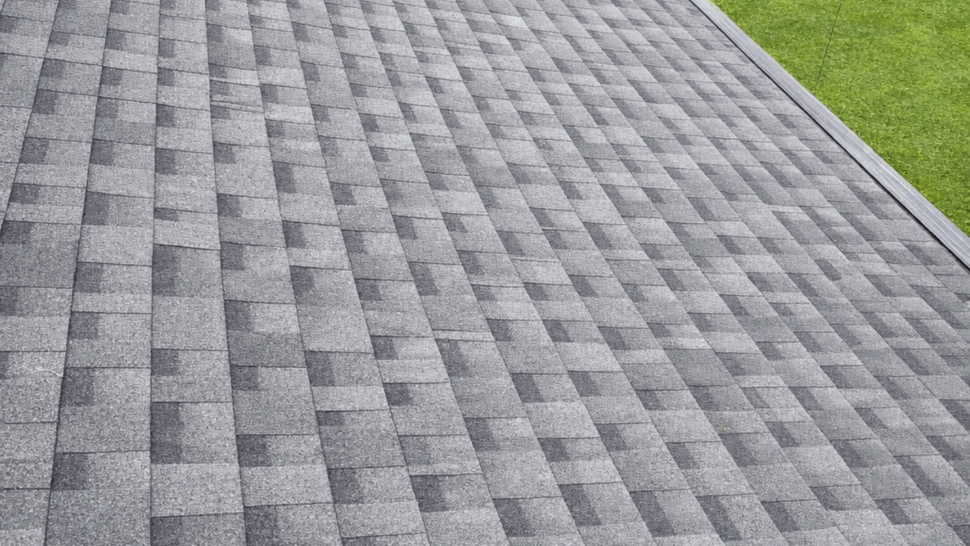 Angled panorama of gray shingle roof slope with vent and eave edge