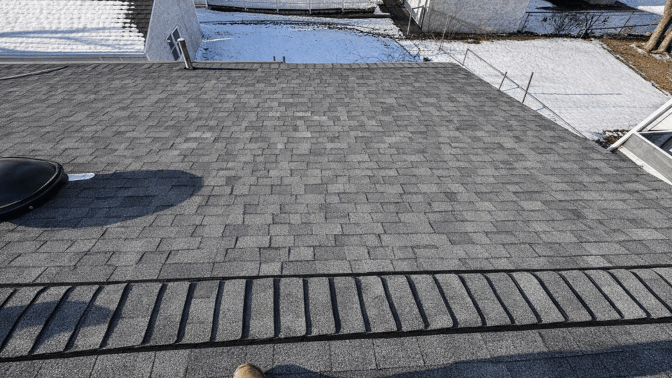 Close-up of asphalt shingles and ridge cap with a worker's boot shadow