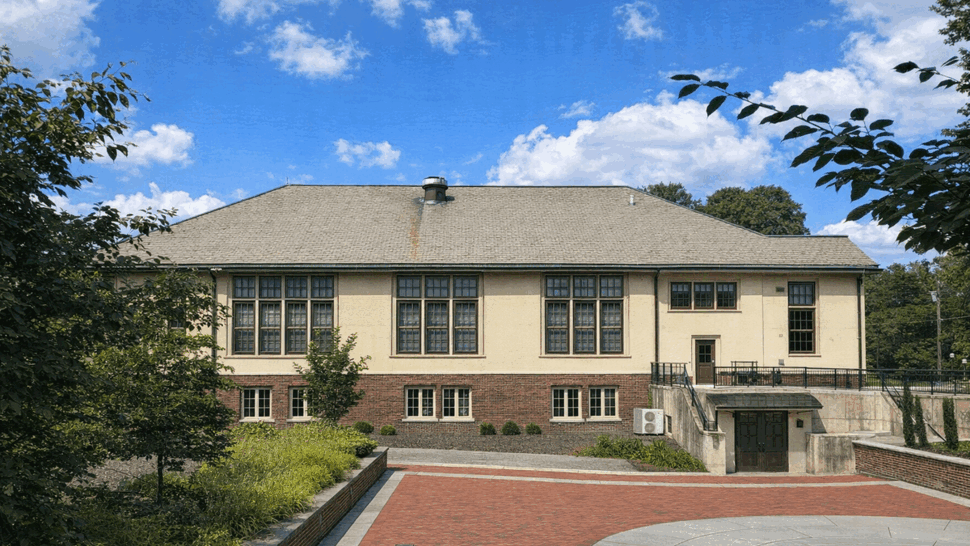 Wide view of a community building with a large hipped roof and brick foundation