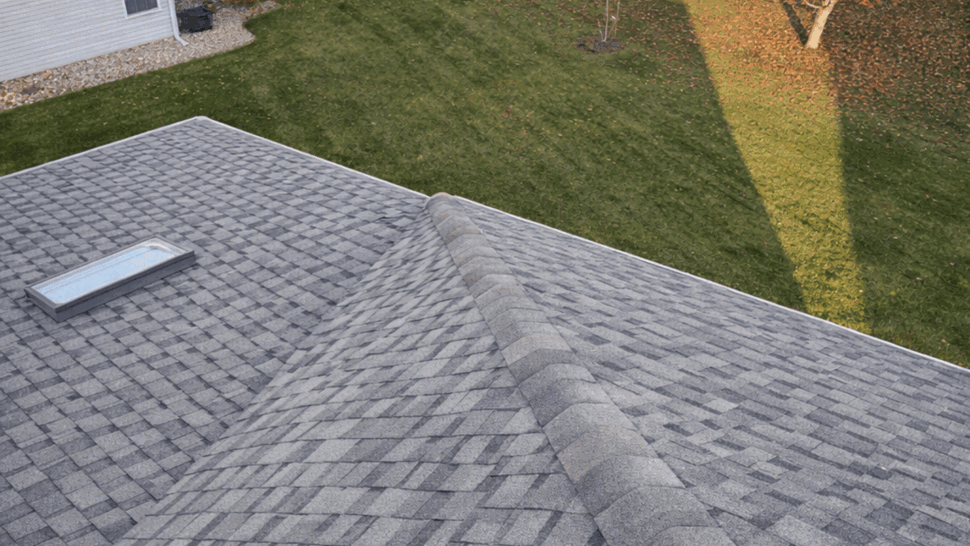 Aerial view of gray shingle roof | Tycos Roofing And Siding Inc Aerial rooftop view of gray asphalt shingles, a skylight, and neighborhood lawns.