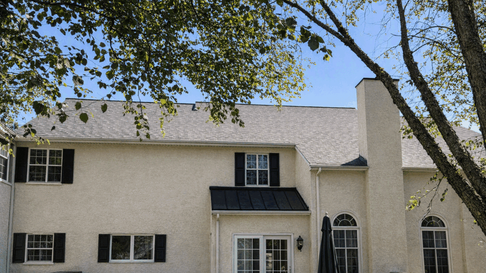 Dormer Roof on Two-Story Home | Tycos Roofing And Siding Inc Two-story home with dormer roof, stucco siding and landscaping under clear blue sky