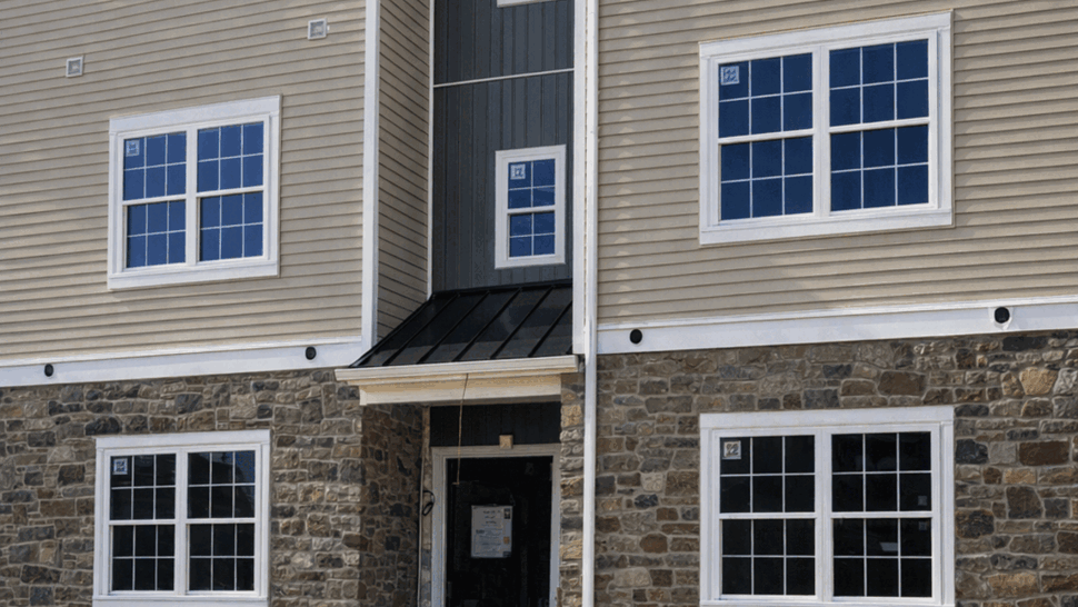 Building entrance with stone veneer, beige siding, white gutters and windows
