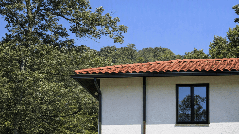 Roofline with dark gutters and window beneath eaves on stucco wall