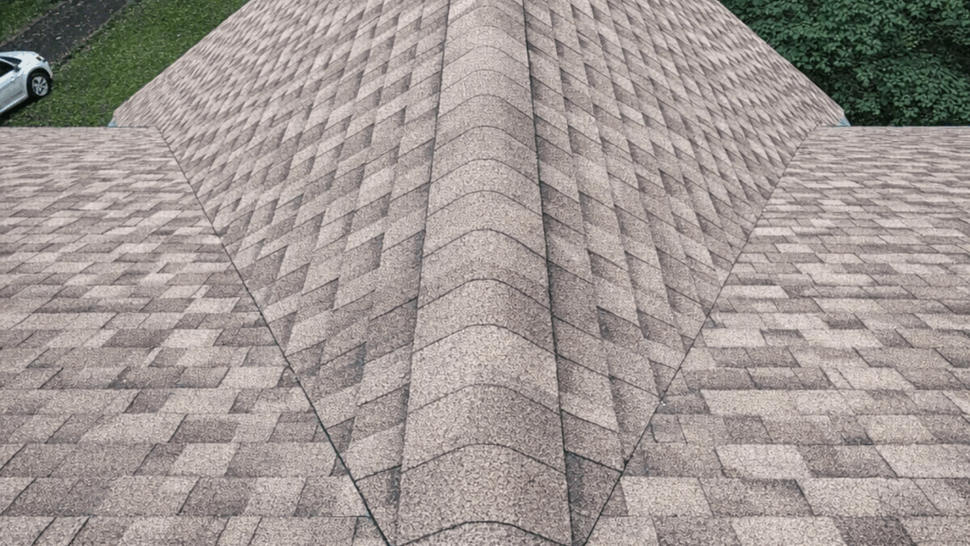 Close-up overhead view of a roof ridge with freshly installed asphalt shingles and a neat ridge cap.