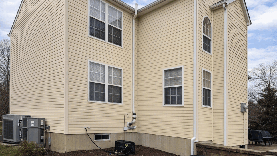 Vinyl Siding Corner with Downspout | Tycos Roofing And Siding Inc Corner of a beige vinyl-sided home showing downspout and double windows
