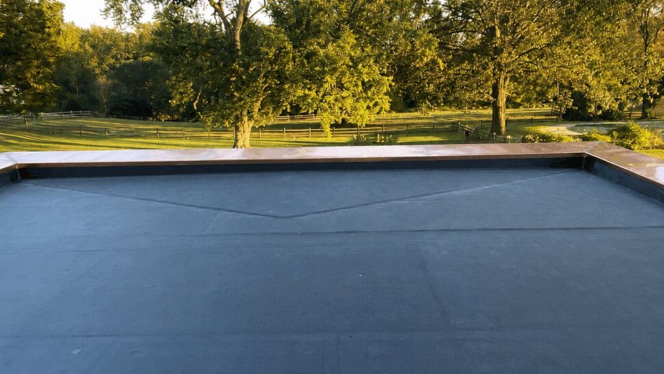 Close-up of a new flat roof membrane with copper edge and trees in background