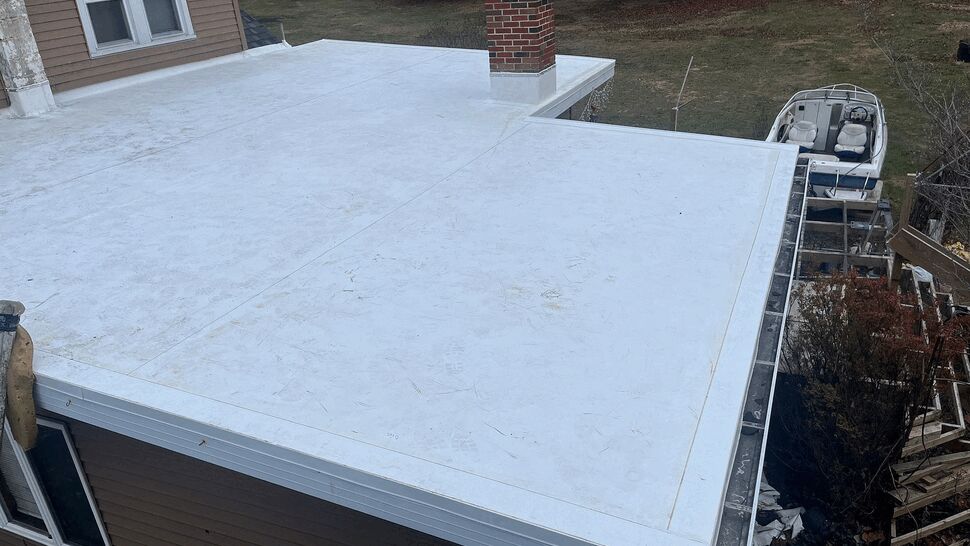 White single-ply flat roof membrane viewed from above with roof edge and gutter