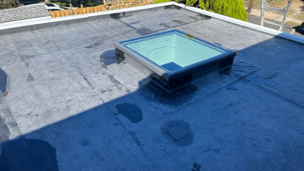 Flat membrane roof with skylight and visible water patches