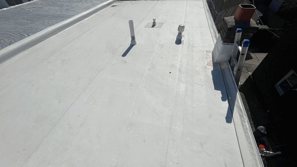 Flat roof showing plumbing vents, ladder and long run of white membrane.