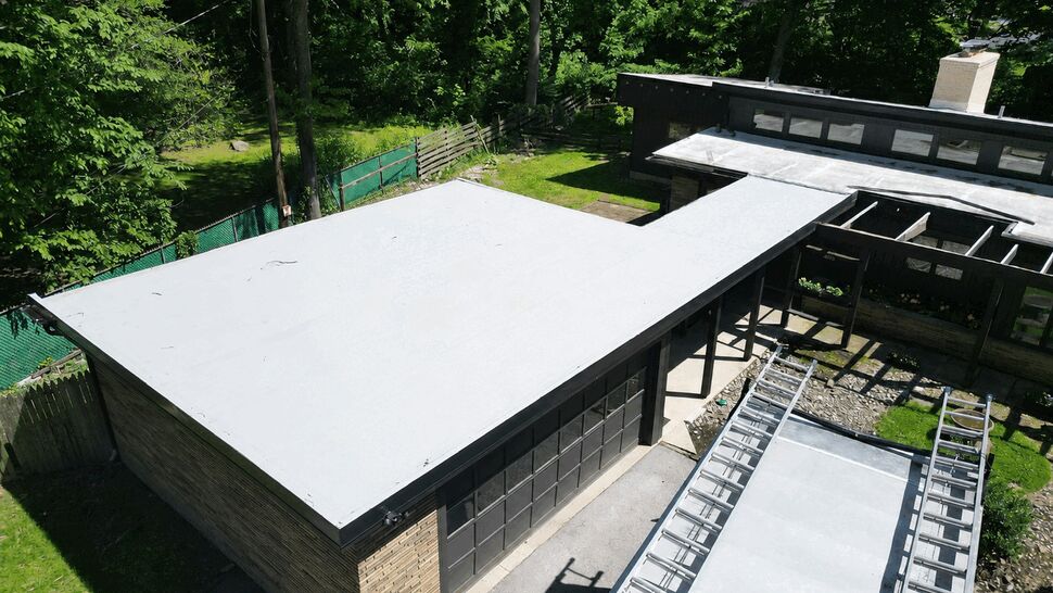 Aerial view of a flat white garage roof with surrounding trees and ladders on driveway