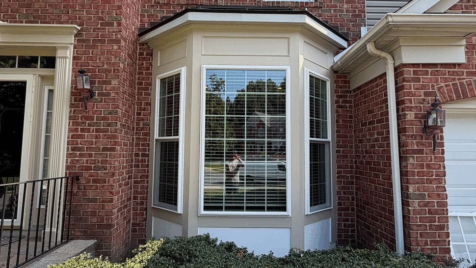 Front view of bay window with brick facade, white trim and shrubs.