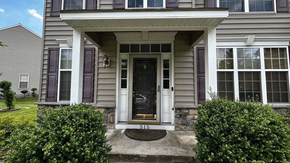 Front porch with glass entry door, sidelights, shrubs and vinyl siding.