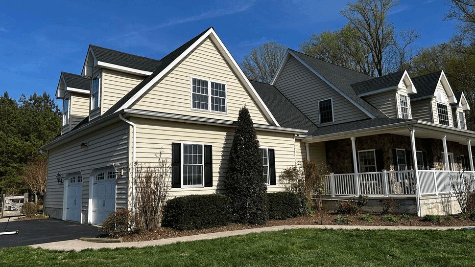 Side view of house with garage, light beige siding and dark roof under blue sky