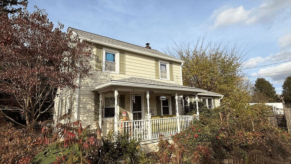 Close view of porch railing, columns, and exterior siding surrounded by overgrown shrubs.
