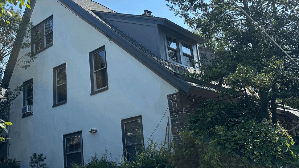 Three-story house exterior with pitched roof, dormer and surrounding trees.