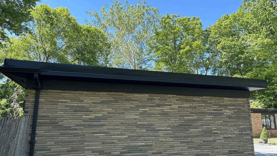 Side view of a garage wall with black gutter and textured brick siding under a blue sky