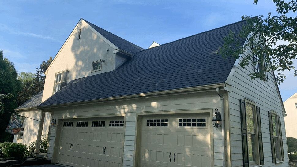 Three-car garage attached to house showing shingled roof, gutters, and beige garage doors.
